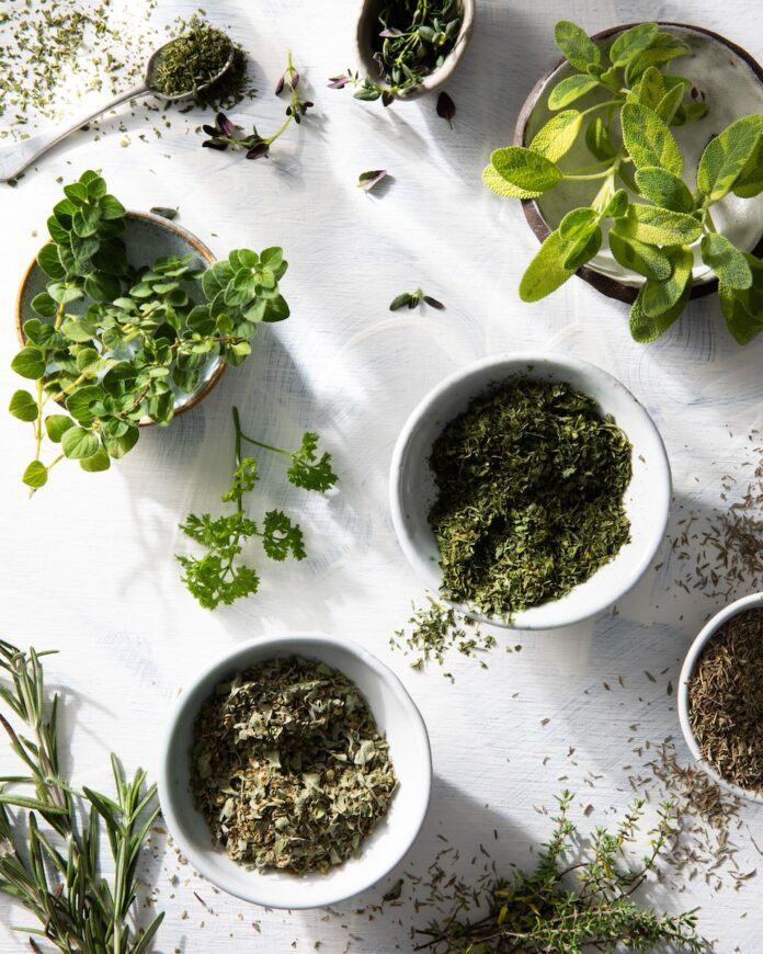 Bowls of various shades of green herbs plated on a white background.