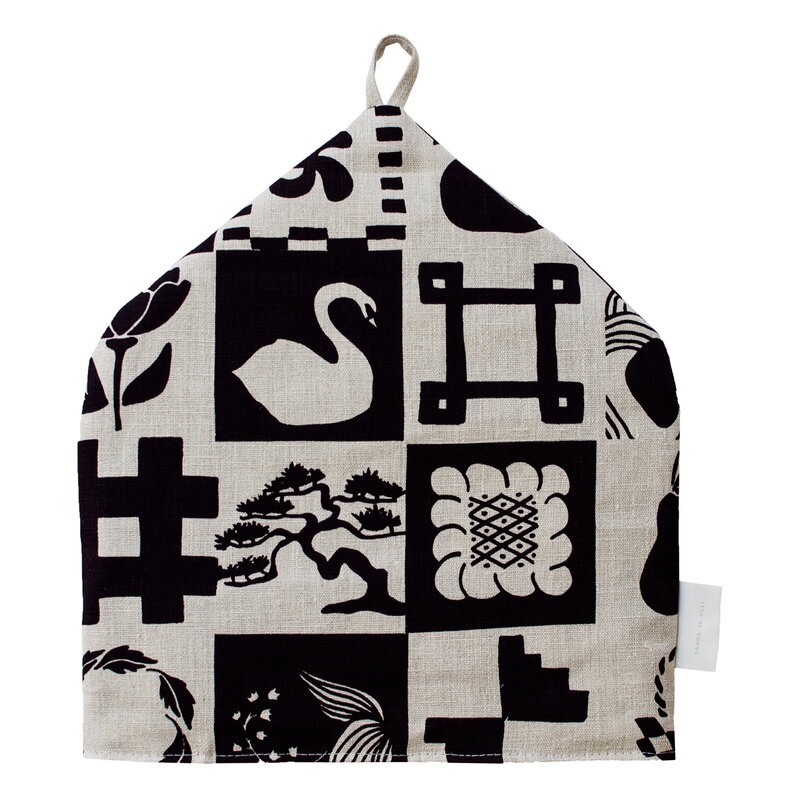 A tea cozy with black and white designs on it including swans and flowers.