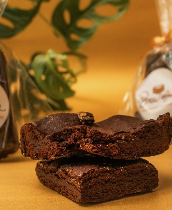 Two olive oil brownies on a yellow background.