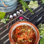dish featuring napa cabbage leaves stuffed with a homemade vegan chorizo mixture, topped with a vibrant red harissa tomato sauce, and surrounded by fresh herbs and vegetables.