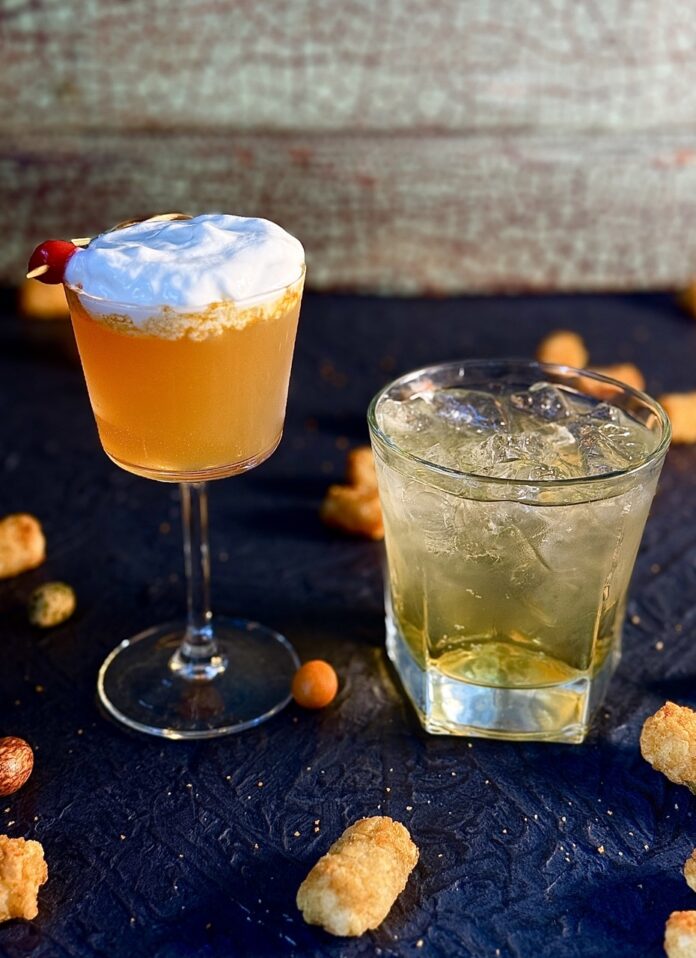 Two Super Bowl cocktails, one for the chiefs and one for the eagles sit on a blue board with tater tots scattered around them.