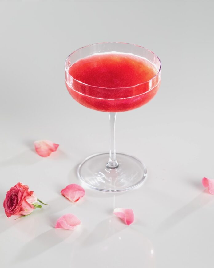 Our Anora cocktail, a raspberry cosmo, on a white background with rose petals.