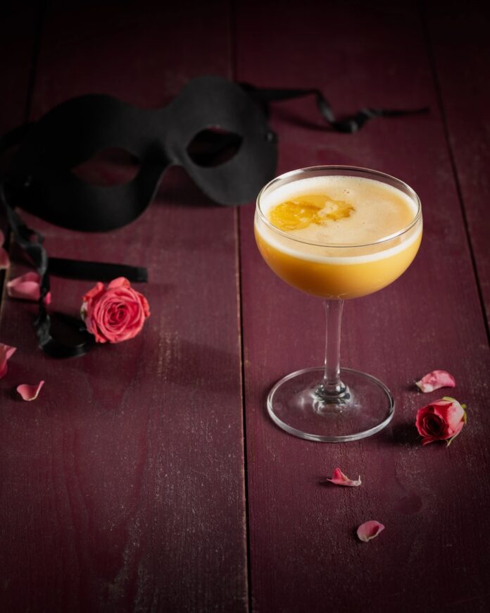A Purim cocktail on a purple background with a mask and some roses.