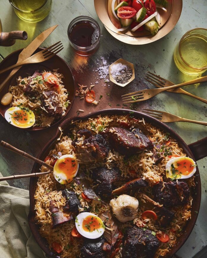 A beef short rib plov for navrus sits in a big dish with rice, beef short rib, and boiled eggs cut in half.