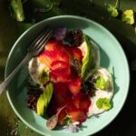 Thinly sliced salmon and beets to made a Beet Gravlax in a teal bowl surrounded by greens.