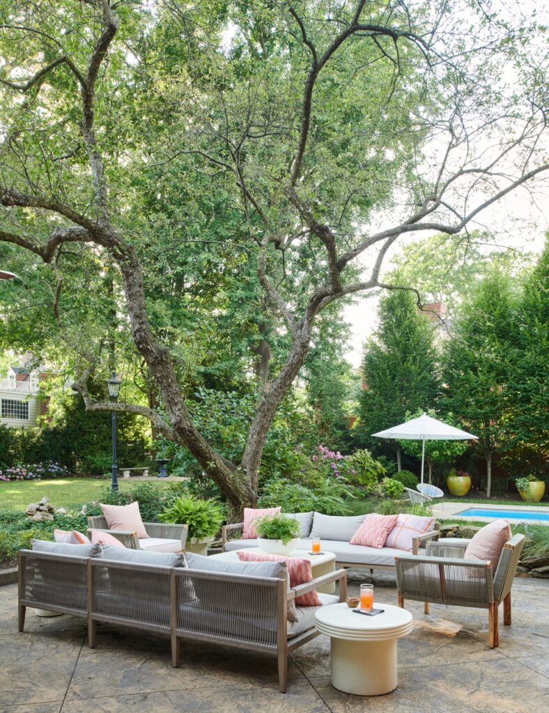 A Betsy Wentz designed patio space with two colorful couches and a chair sitting on a stone patio with a large tree nearby.