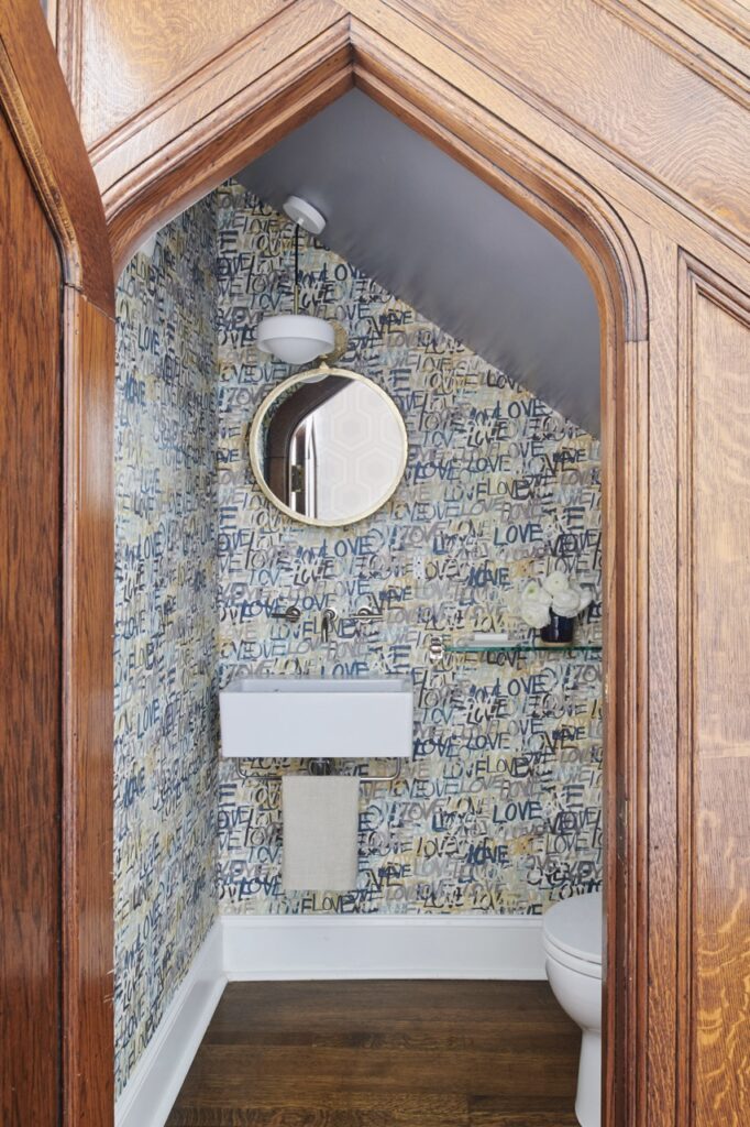 A bathroom with a pattern wallpaper inside a brown archway designed by Betsy Wentz.