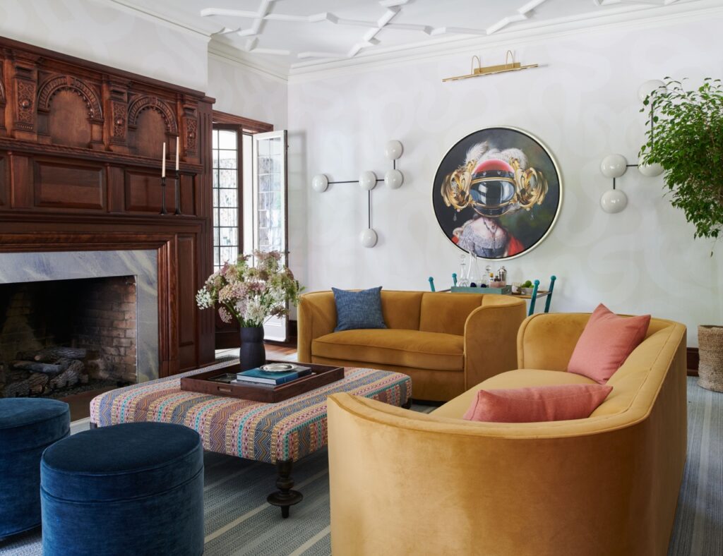 A yellow L-shaped couch sits in a living space designed by Betsy Wentz with a fireplace and painting on the white wall.