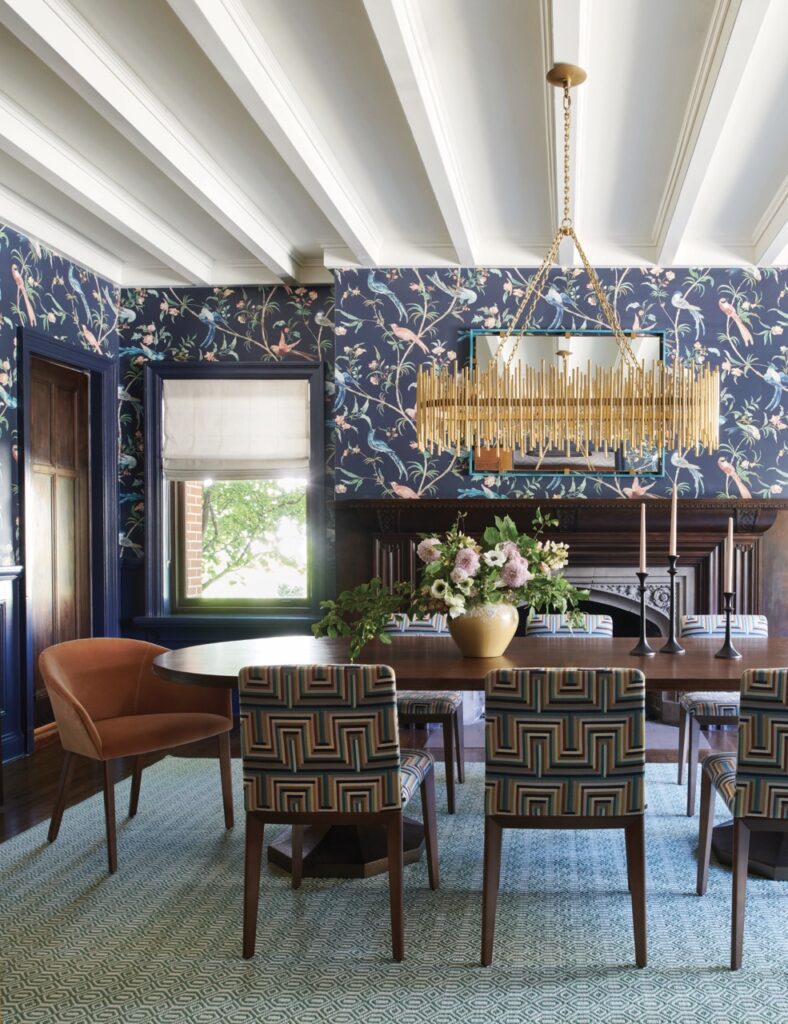 A dining space by Betsy Wentz with a blue bird pattern wall and dark wood table in the center with blueish-backed chairs to match the wall.