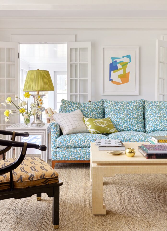 A light blue patterned couch with a green pillow on it and a green lamp to the left sitting in a living room.