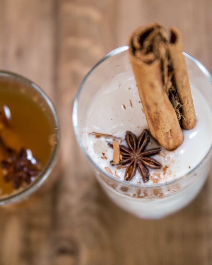 A glass of cremas with anise and a cinnamon stick in it.