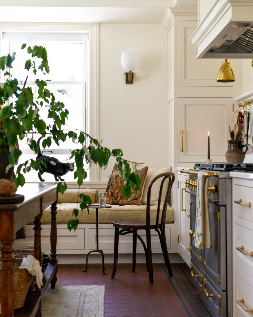 Part of a Cruze Architects designed kitchen with a nook reading area, plants on the dining table, and a metallic stove between white counters.