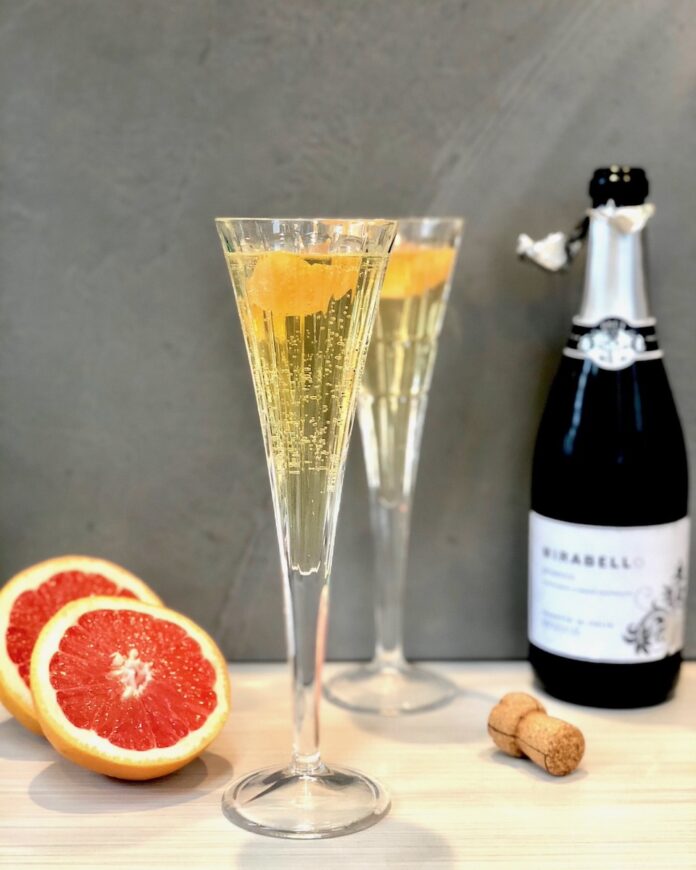 A Greyhound 75, two small glasses with a grapefruit and a Prosecco bottle beside it.