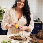 Lisa Theuer stands in front of her Pomegranate Molasses Roasted Lamb Shoulder in a white-walled kitchen.