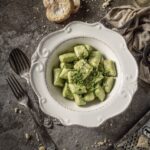 A white bowl holds Potato and Pea Gnocchi in a green color with two forks sitting beside the bowl and bread sitting above it.
