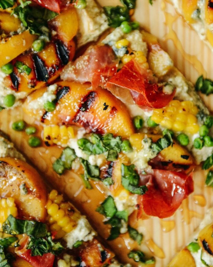 A savory and sweet dinner pie with puff pastry, cheese, corn, sweet peas, prosciutto, and grilled peaches.
