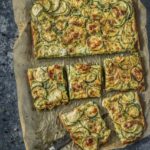 A piece of parchment paper sits on a counter top with square slices of Italian Scarpaccia scattered on the paper.