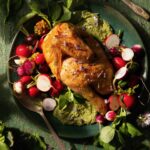 A green plate on a green surface plates spring chicken with a fava shoot pesto and half-cut radishes.