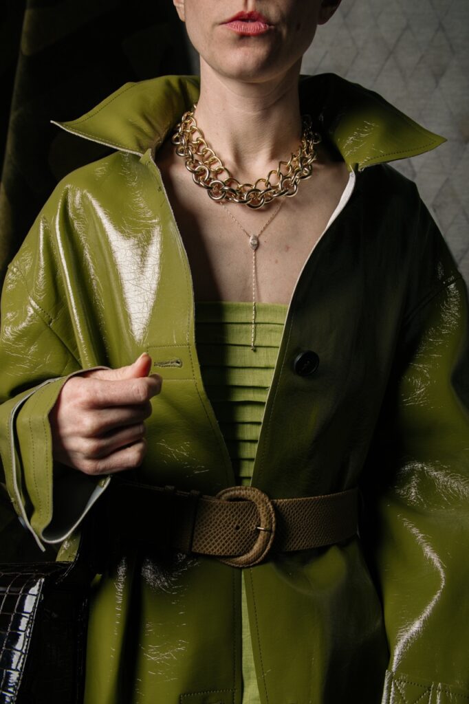 A woman wearing a green spring fashion leather coat with a chunk chain neckalce.