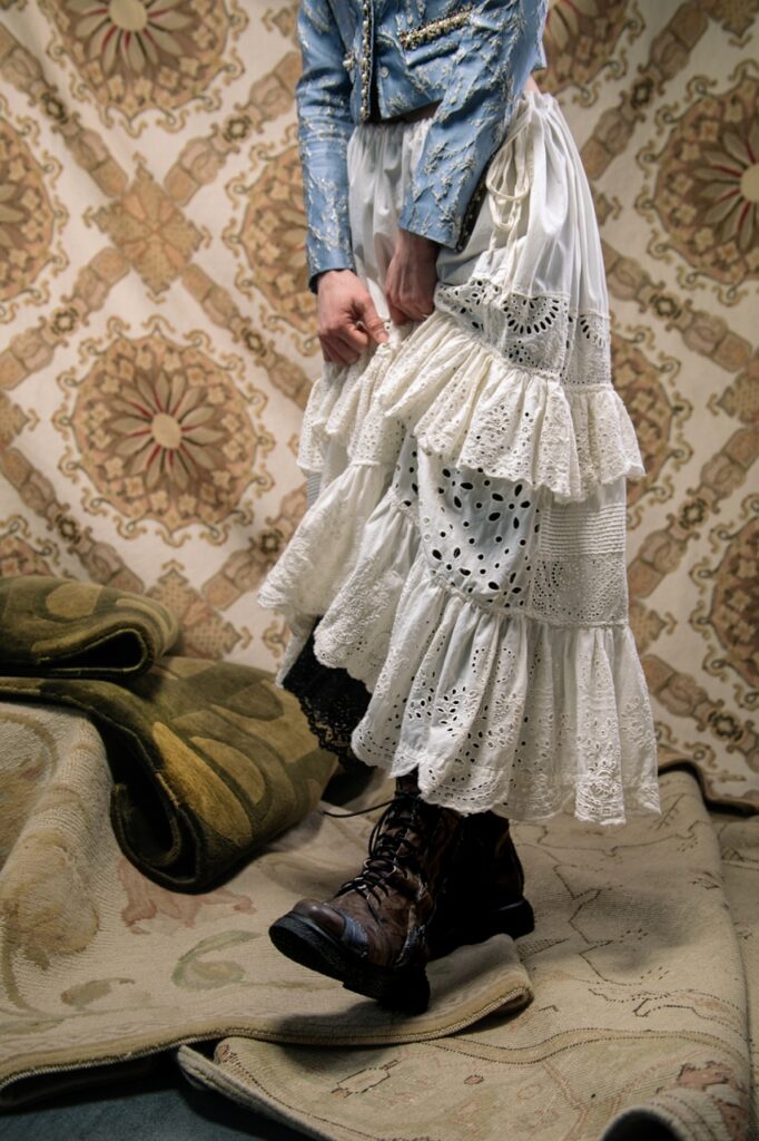 A woman in a white skirt pulls up her skirt to reveal black boots beneath it.