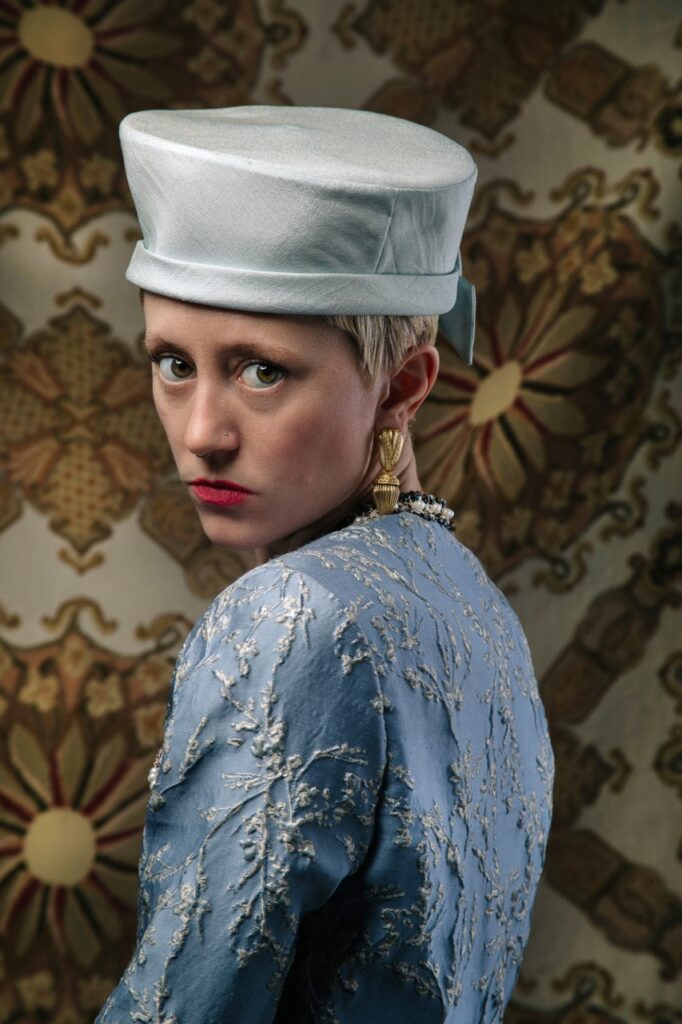 A blonde woman in a pale blue hat and blue oriental top.