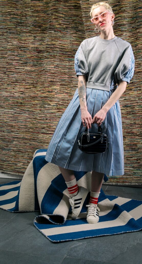 A woman in a puffy fashion trend shirt and blue plaid skirt wit white sneakers on.