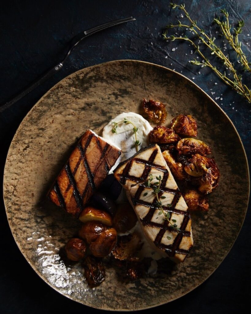 A swordfish with pork belly dish on a black plate.