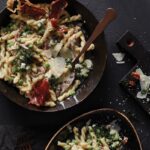 Gemelli, prosciutto and peas in a saucepan on a black background.