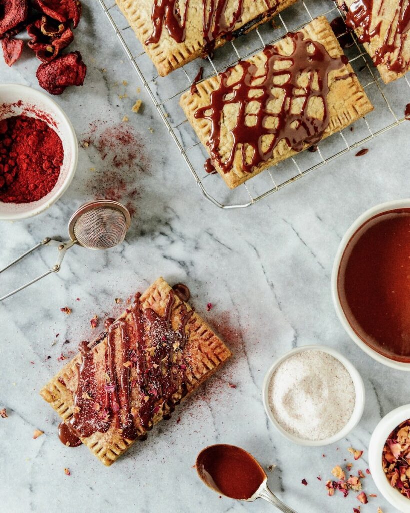Cherry chocolate pop tarts sit on a cooking tray as they get drizzled with chocolate.