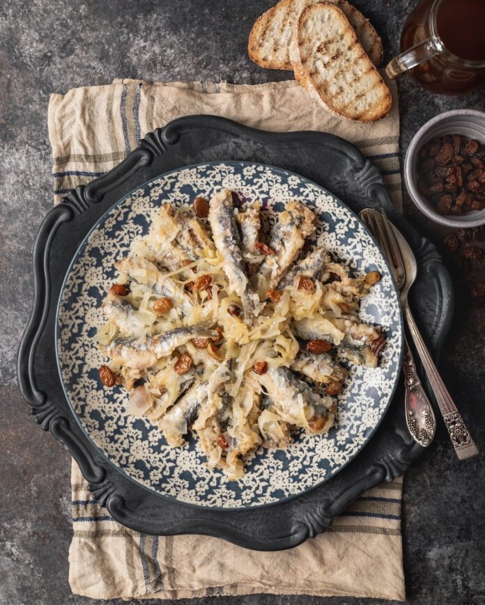 Sarde in Saor on a porcelain plate set on a rustic table.