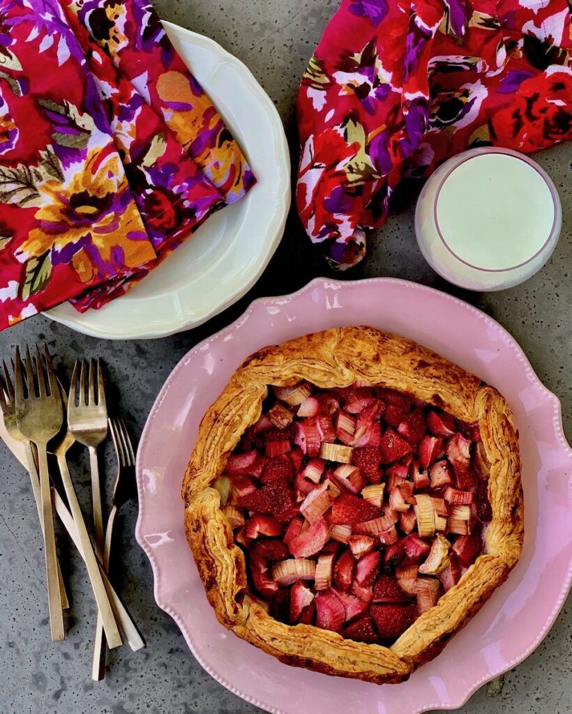 A strawberry rhubarb tart on a white background with dinnerware.
