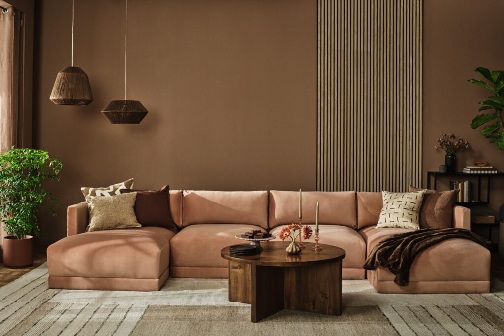 A brown sectional couch sits against a brown living room wall with a neutral carpet below.