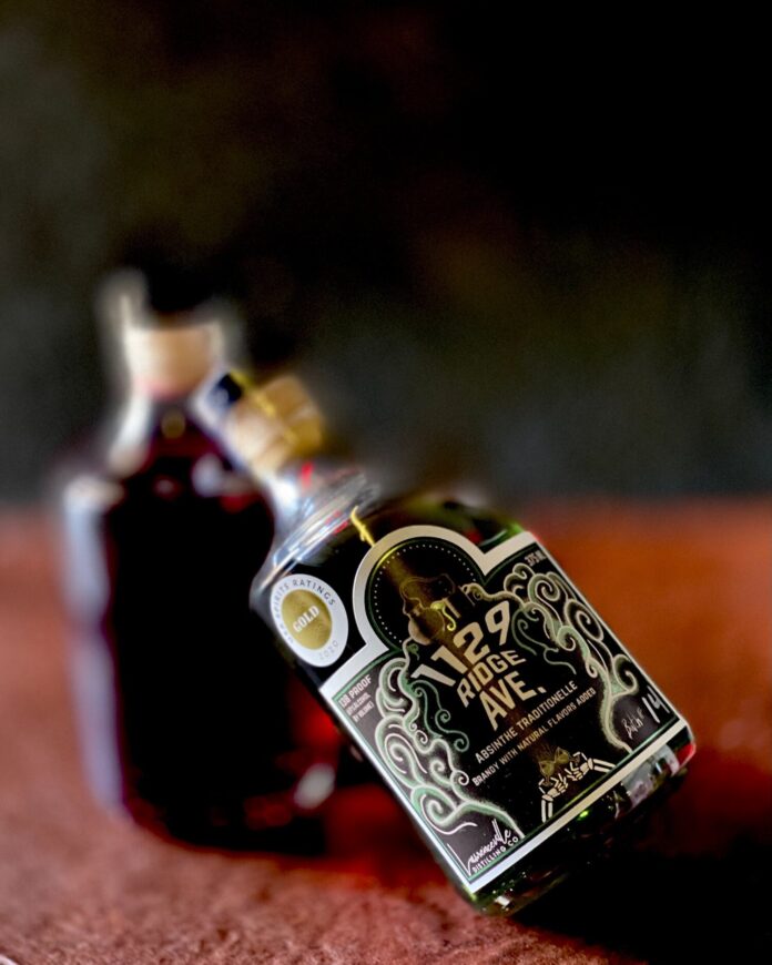 A bottle of green absinthe to make a gimlet with sits on a wood table, leaning against another bottle of absinthe.