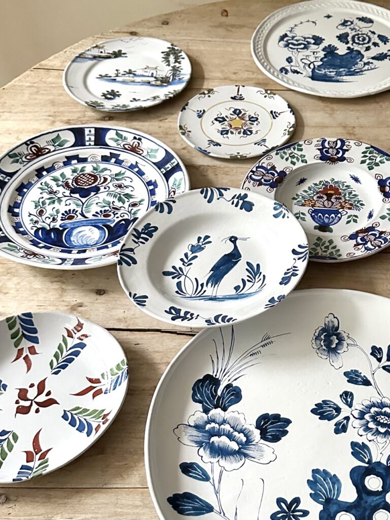 Various white plates with blue delftware designs sit scattered on a cream picnic table.