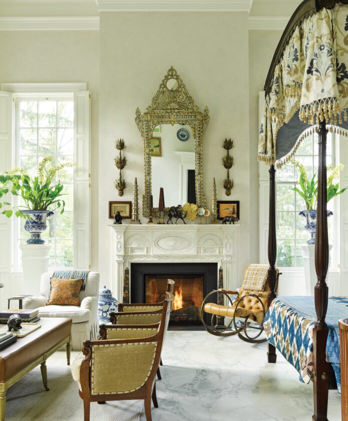 Bunny Williams design of a living room with a mirror on the fireplace and vintage furniture around the room.