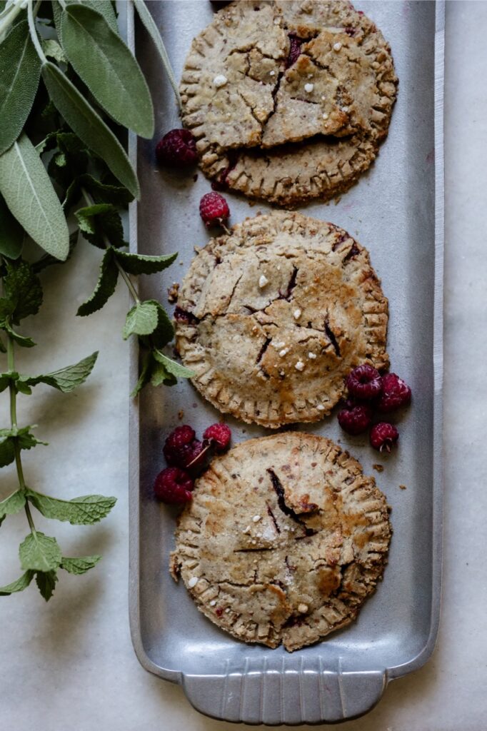 Three raspberry and cream hand pies sit on a platter made from foraged backyard raspberries.