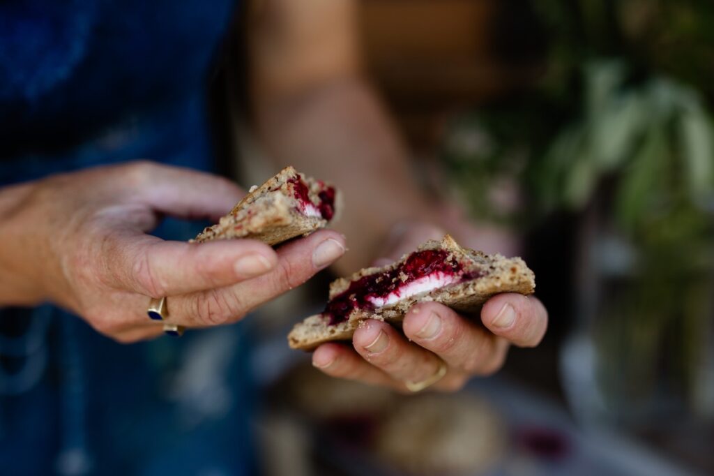 A person breaks open a raspberries and cream hand pie showing the red and white layers inside.