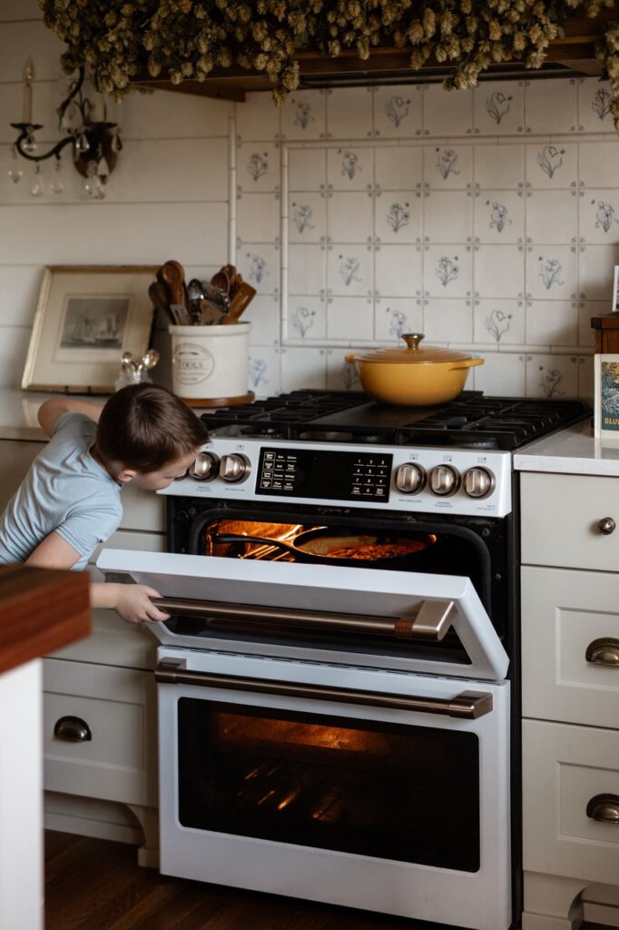 A boy checks the over where blueberries bake into a dutch baby.