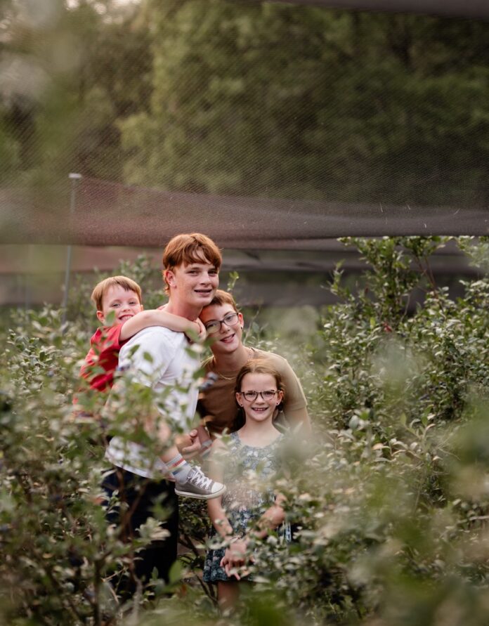 A group of siblings gather in a field for foraging blueberries from various bushes.
