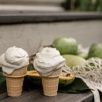 Two pawpaw fruit ice cream cones sit in front of a pile of pawpaw fruits.