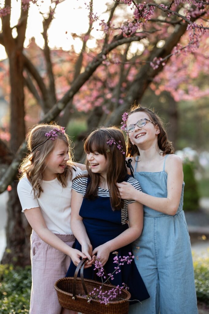 Three young girls laugh under a redbud tree.