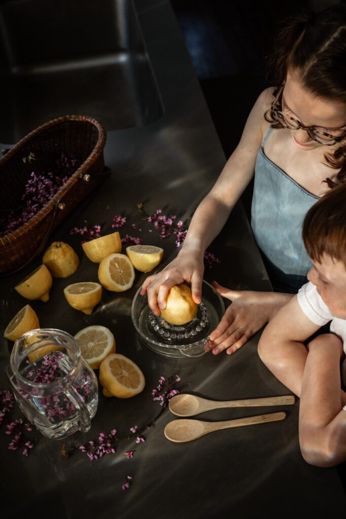 A young girl juices halved lemons as a young boy in a white shirt watches.