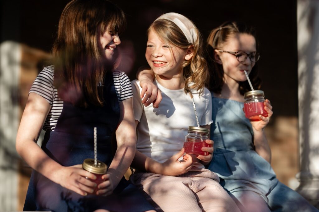 Three young girls sit arm in arm sipping on redbud lemonade in mason jars