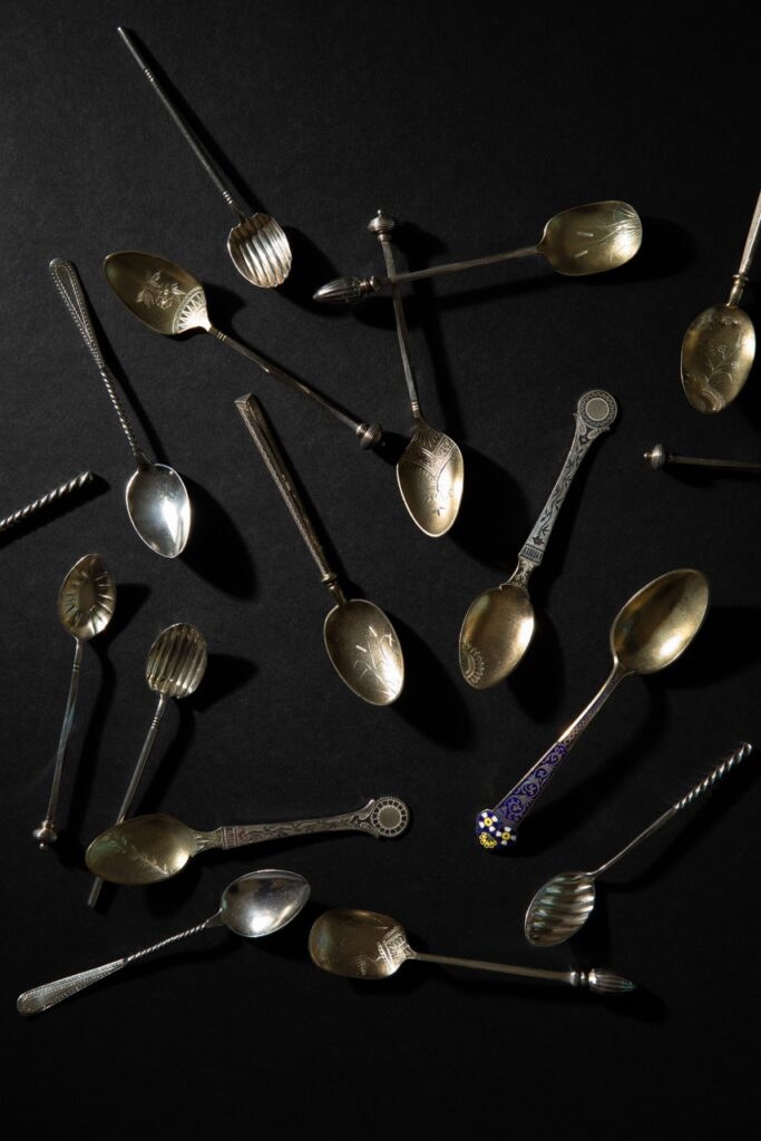 A bunch of coffee spoons from the Frick's tableware collection sit scattered on a black table.