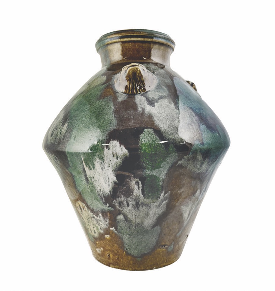A green, blue, and brown vase in an almost diamond shape sits on a white background.