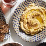 A lemon artichoke hummus sits in a polka dot blue and white bowl on a white picnic table.
