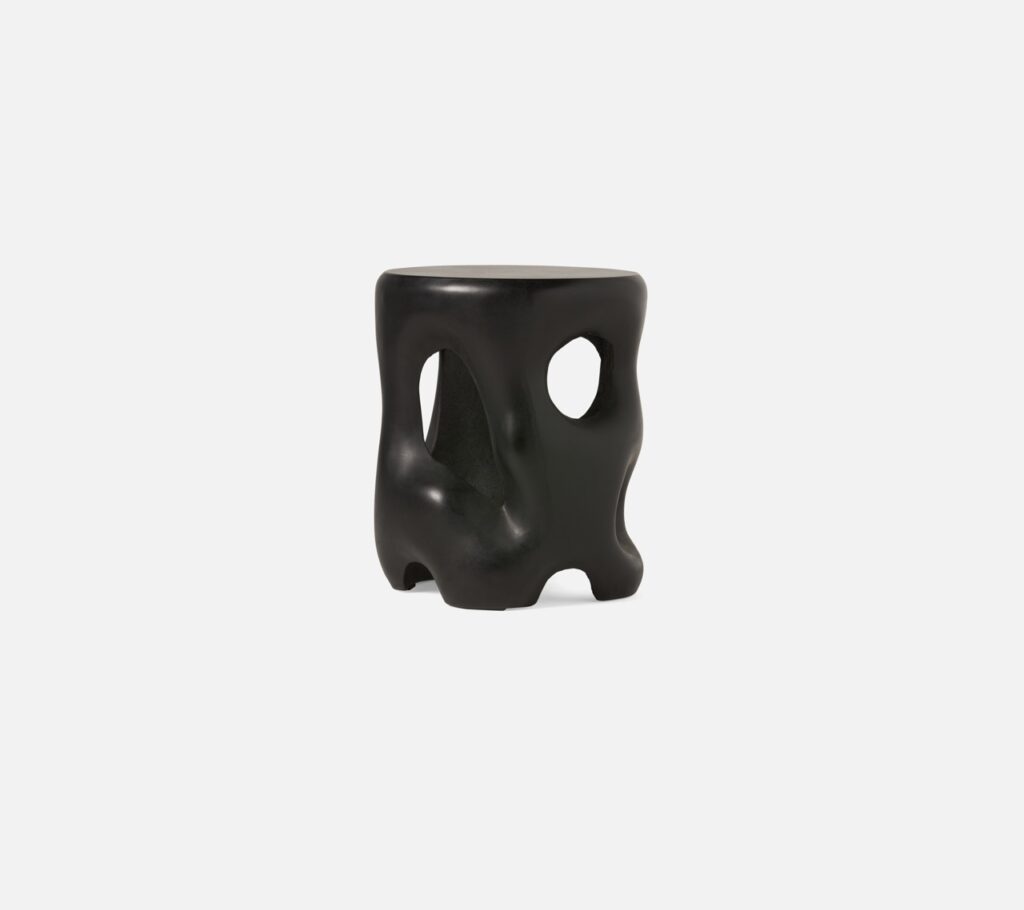 A black stool in an odd shape sits on a white abckground.
