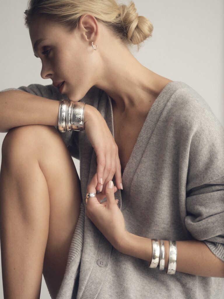 A woman in a grey sweater wears various silver bracelets. 