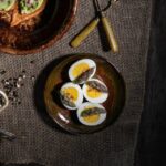 A small brown plate holds four deviled eggs topped with paprika as a plate of pea puree triangles sit in the upper left corner.
