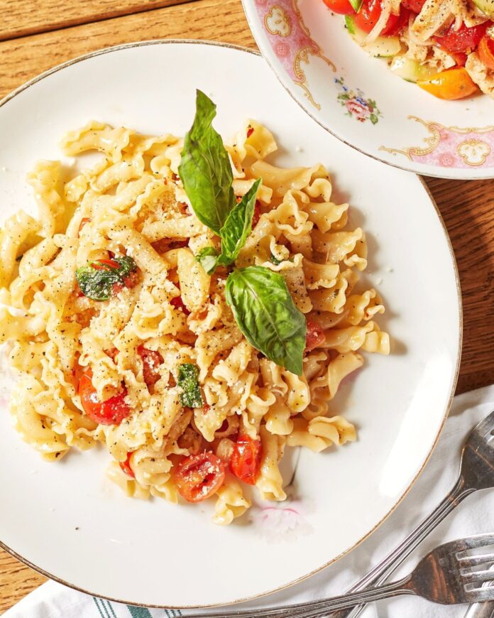 A white plate holds Spaghetti Aglio e Olio with oodles, tomatoes, and basil on top.